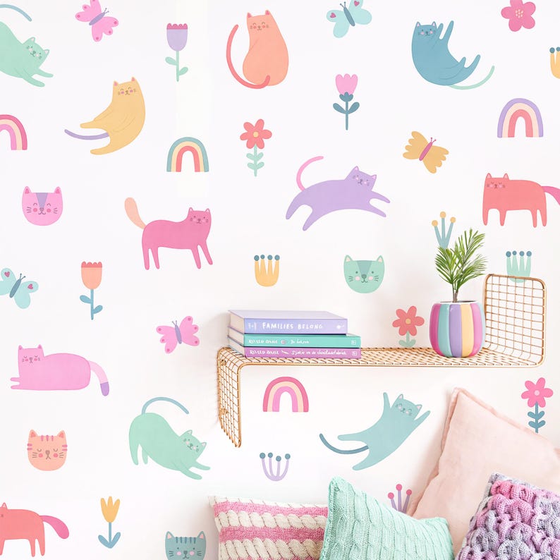 May include: A white wall with colorful cat and flower decals. The decals are in various shades of pink, blue, green, yellow, and orange. There are also rainbow decals and butterflies. The decals are arranged in a random pattern on the wall.