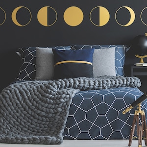 Puede incluir: Una cama azul oscuro con una manta de punto gris y una funda nórdica con estampado geométrico. La cabecera es negra y tiene pegatinas de fases lunares doradas. Una lámpara de globo negro y un telescopio están en una mesita de noche negra.