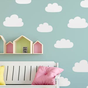 May include: A white bench with a white slatted back and a light blue wall with white cloud cutouts. The bench has two yellow and two pink pillows. There are wooden shelves above the bench with a small black sign that says "If you're waiting for the perfect moment, this is it."