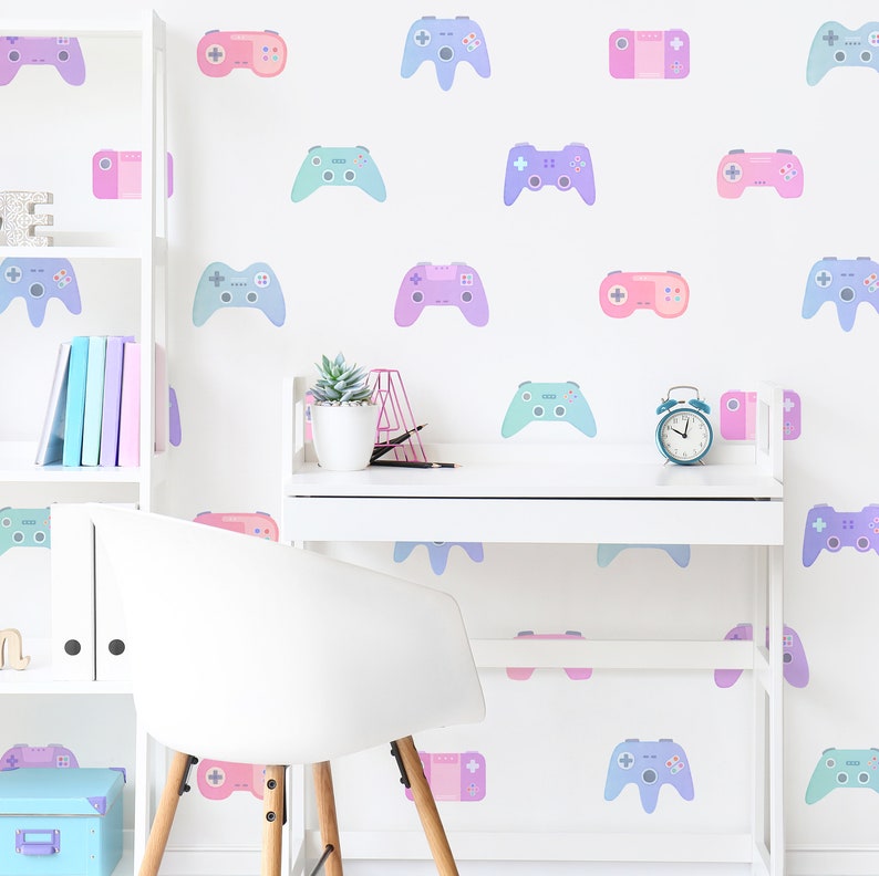 May include: A white desk with a white chair in front of it. The wall behind the desk is decorated with pastel-colored game controller stickers. There is a small alarm clock on the desk.