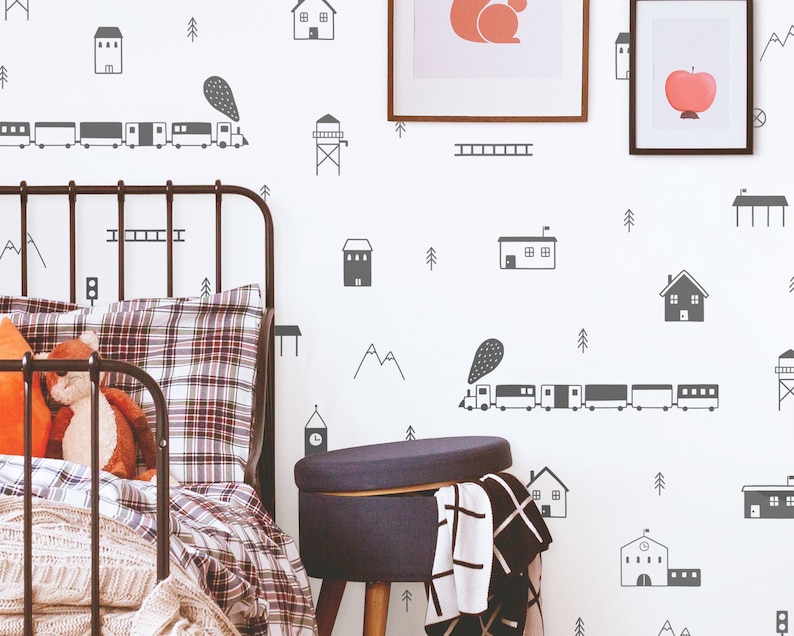 May include: A white wall with black and gray train, house, and tree decals. A black metal bed frame with a plaid comforter and a gray ottoman are in the foreground.