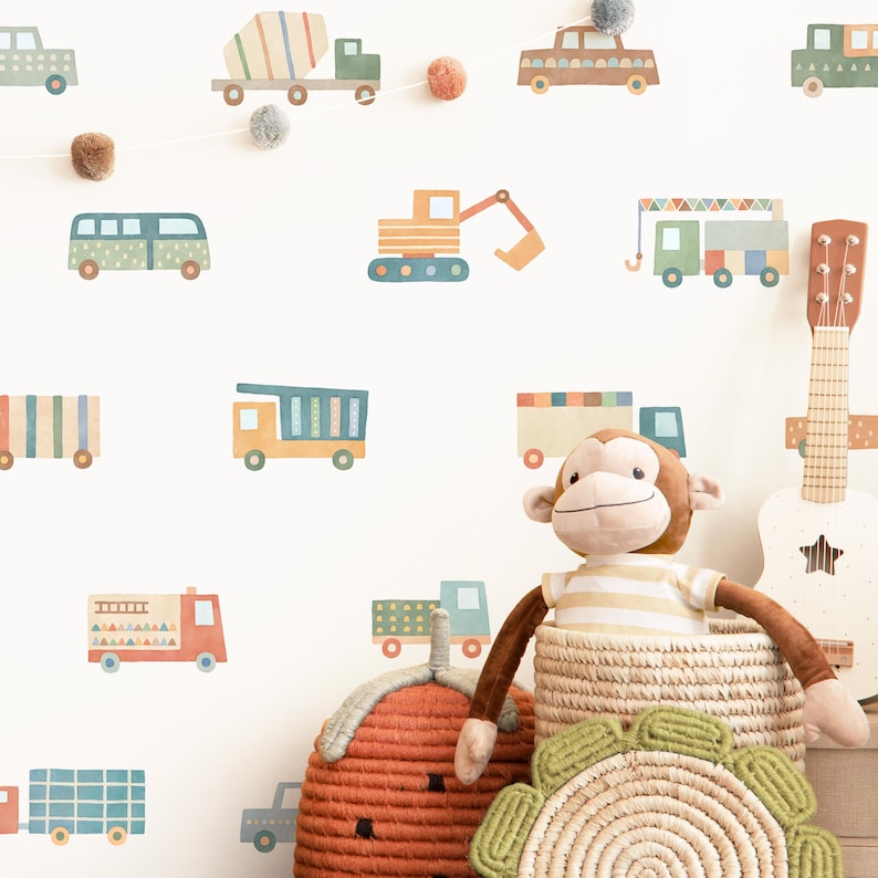 May include: A white wall with colorful cartoon vehicle decals, including a cement mixer, a fire truck, a dump truck, a bus, and an excavator. There is a stuffed monkey toy sitting in front of a wicker basket.