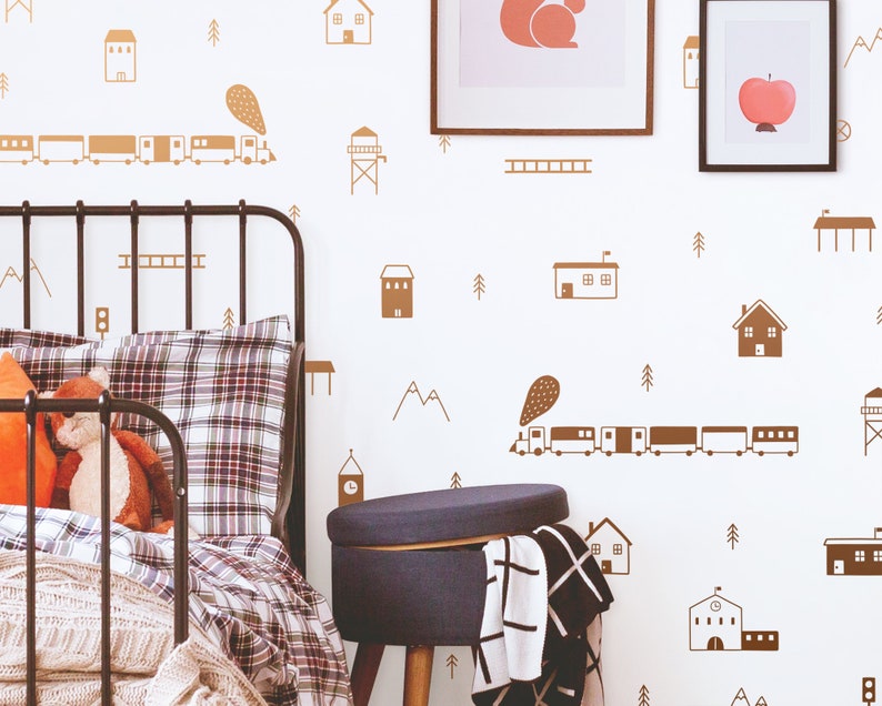 May include: A brown and white train with a brown and white smoke plume travels across a white wall with brown house and tree illustrations. A black metal bed frame with a plaid comforter and a blue ottoman are in the foreground.