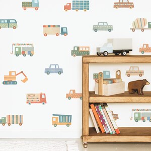 May include: A white wall with colorful vehicle decals, including a truck, a crane, a fire truck, a car, and an excavator. A wooden shelf with books and a toy truck is in the lower right corner.