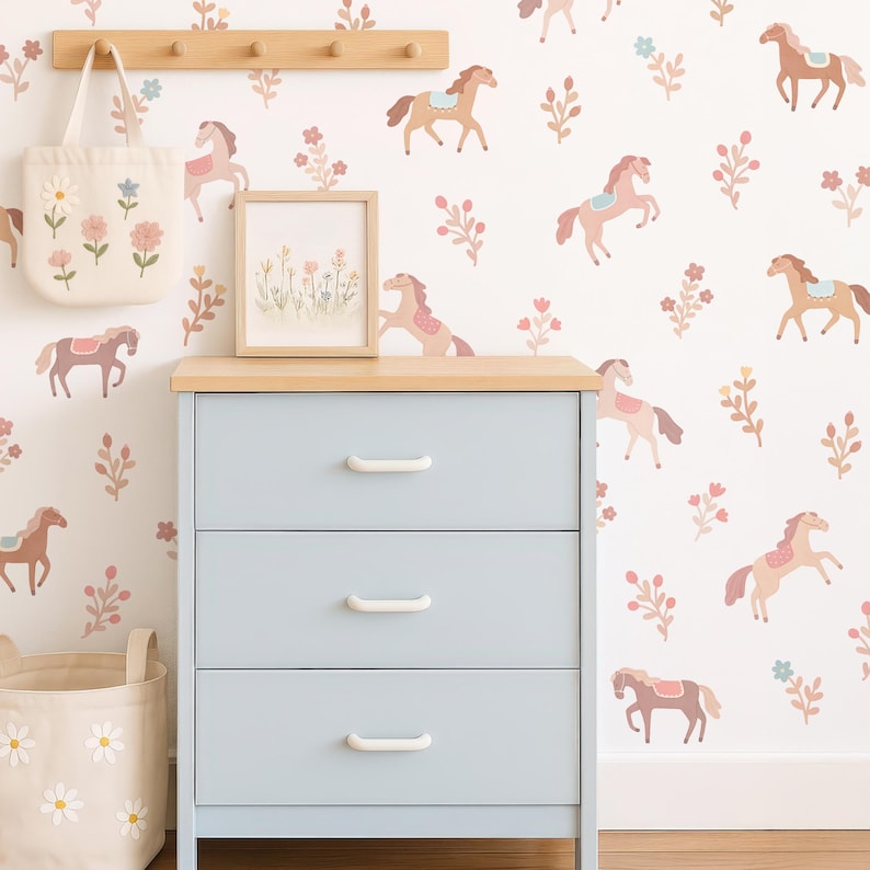 May include: A light blue three-drawer dresser with white handles, a wooden top, and a white wall decorated with horse and floral decals. A tote bag with floral embroidery and a framed picture are also visible.