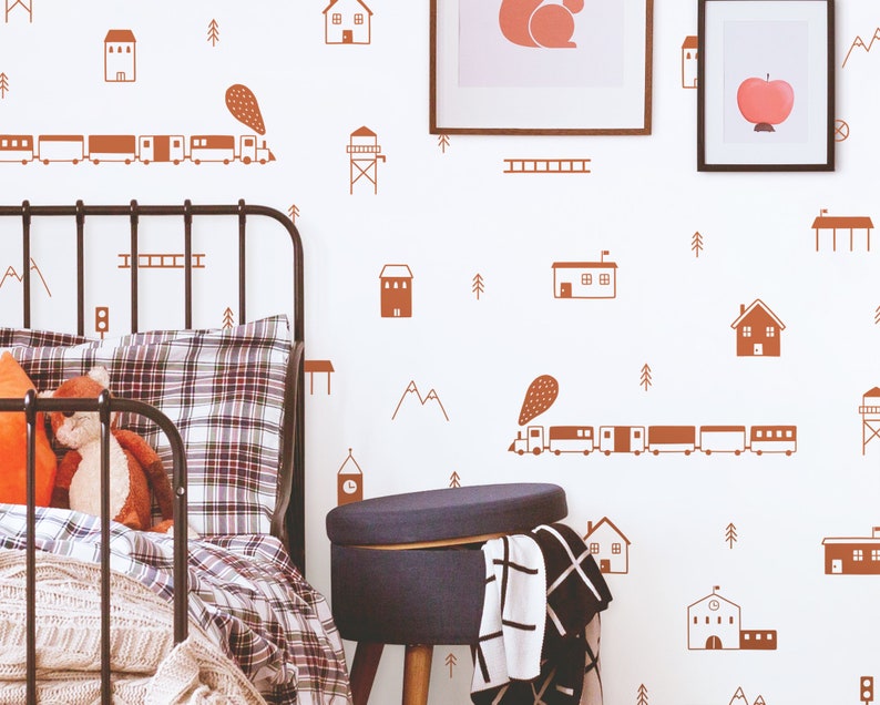 May include: A white wall with brown train, house, and tree decals. A black metal bed frame with a plaid comforter and a blue ottoman are in the foreground.