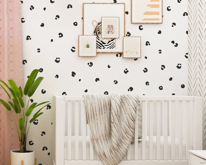May include: A white crib with a white blanket and a black and white leopard print wallpaper. There is a green plant in a pot on the left side of the image.