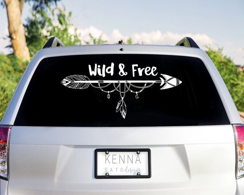 May include: A white car with a black rear window. The window has a white decal with an arrow and the text "Wild & Free". The car has a license plate that reads "KENNA SATODESIGNS".