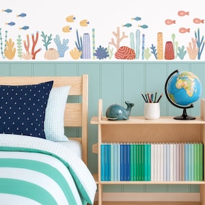Puede incluir: Un adhesivo de pared que muestra una colorida escena de arrecife de coral submarino con varios peces, plantas marinas y formaciones de coral en tonos azul, naranja, amarillo y verde, dispuestos en un patrón de borde horizontal.