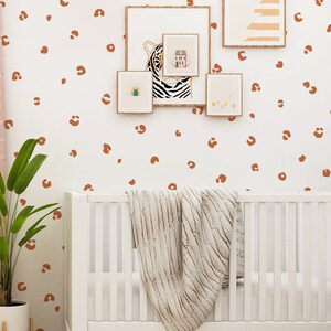 May include: A white crib with a white blanket and a white wall with brown leopard print decals. There are framed pictures on the wall above the crib.