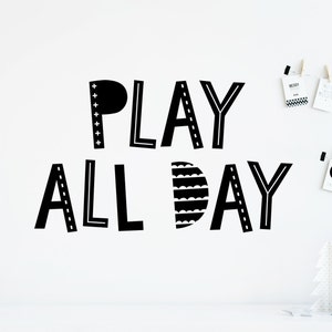 Puede incluir: Un adhesivo de pared negro con el texto PLAY ALL DAY en una fuente estilizada. Las letras P, L, A y Y incorporan varios patrones, incluyendo signos m&aacute;s, l&iacute;neas discontinuas y ondas festoneadas horizontales en las formas.