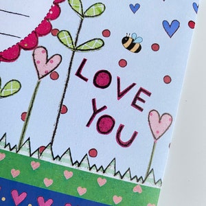 May include: A light blue card with a pink heart, green leaves, and a bee. The card says "LOVE YOU" in pink letters.