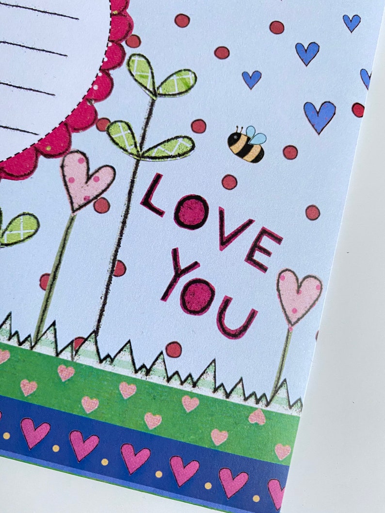 May include: A light blue card with a pink heart, green leaves, and a bee. The card says "LOVE YOU" in pink letters.