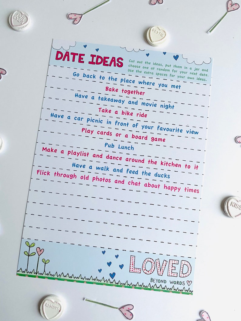 May include: A white card with blue and pink hearts and the text "Date Ideas" printed on it. The card has a list of date ideas, such as "Go back to the place where you met" and "Have a walk and feed the ducks". The card also has the text "Loved Beyond Words" printed on it.