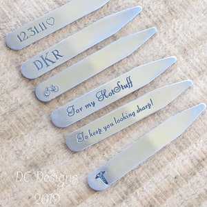 May include: Six silver collar stays with various engraved designs. The designs include a heart with the date 12.31.11, the initials DKR, a bicycle, the text "For my HotStuff", the text "To keep you looking sharp!" and a medical symbol.