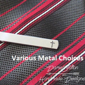 May include: Silver tie clip with a small cross design. The tie clip is on a black and red striped tie. The text "Various Metal Choices" is below the tie clip. The text "Dame Creation 2017 Handmade Designs" is below the text "Various Metal Choices".