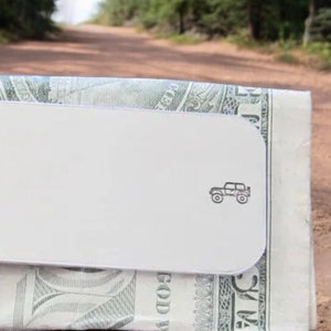 Peut inclure: Un porte-monnaie en argent avec une petite silhouette noire de Jeep sur le devant. Le porte-monnaie est en train de tenir un billet de dollar.