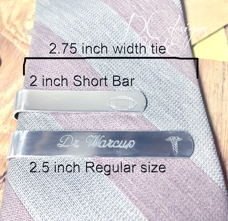 May include: Two silver tie bars on a striped tie. The top bar is 2 inches long and has a football design. The bottom bar is 2.5 inches long and has the text "Dr. Warcup" and a medical symbol.