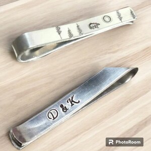 May include: Two silver tie clips. One has a design of trees and a bear with the text "D & K" engraved on the other.