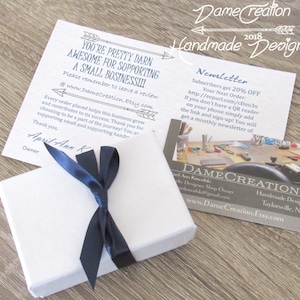 May include: A white gift box with a navy blue ribbon tied in a bow. The box is sitting on a wooden surface. A thank you note is visible in the background with the text "You're pretty darn awesome for supporting a small business!!!" and "www.DameCreation.Etsy.com".