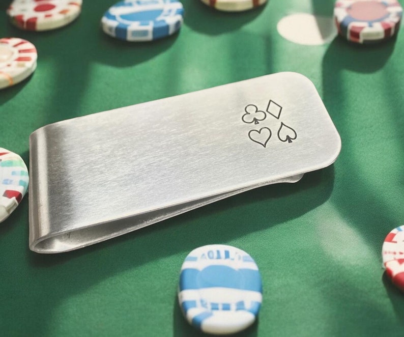 May include: A silver money clip with a design of four playing card suits: a diamond, a club, a heart, and a spade.