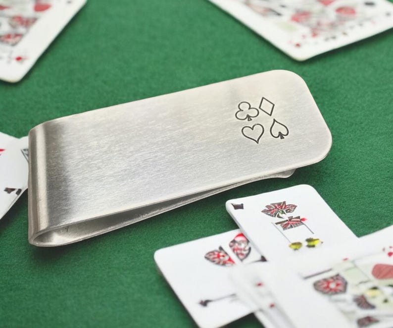 May include: A silver money clip with a design of four playing card suits: a diamond, a club, a heart, and a spade.