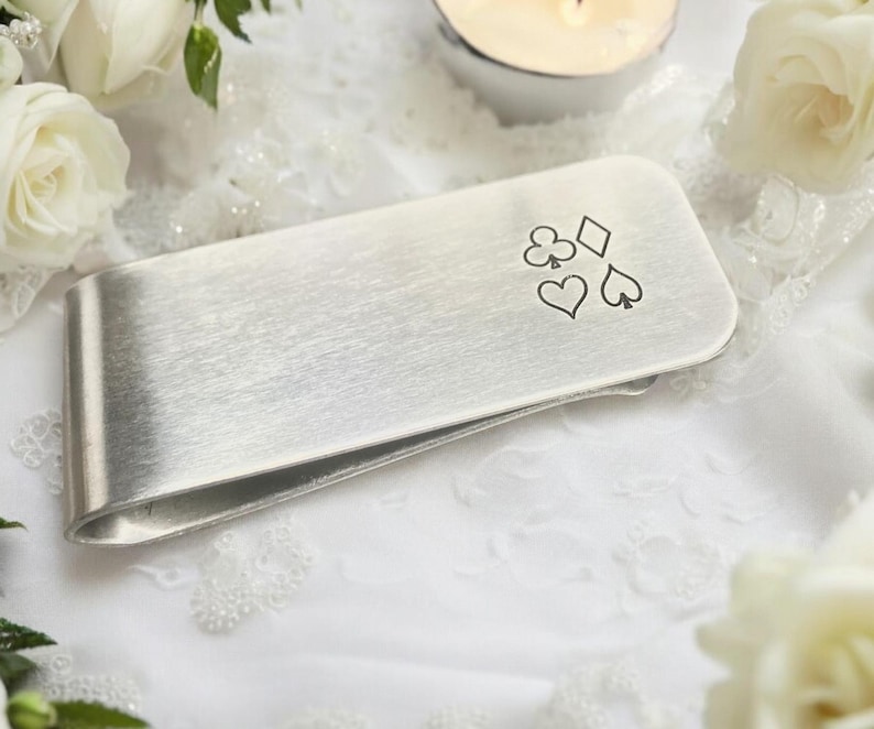 May include: Silver money clip with a brushed finish and an engraved design of four playing card suits: clubs, diamonds, hearts, and spades.