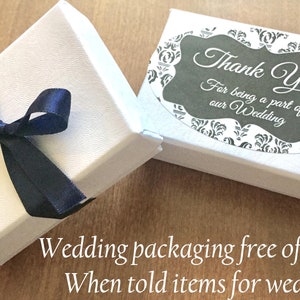 K&ouml;nnte beinhalten: Zwei wei&szlig;e Geschenkboxen, eine davon mit einem dunkelblauen Band. Die Box rechts hat einen Aufkleber mit der Aufschrift "Vielen Dank, dass Sie Teil unserer Hochzeit waren".