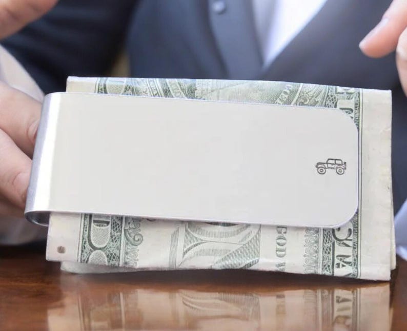 Peut inclure: Un porte-monnaie en argent avec un petit dessin de voiture sur le devant. Le porte-monnaie contient une pile de billets de dollars am&eacute;ricains.