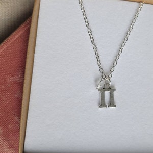 May include: Silver necklace with a Gemini zodiac symbol charm. The charm is a simple, stylized representation of the Gemini symbol.