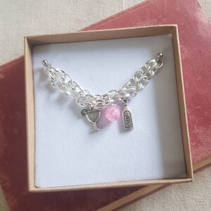 May include: A silver charm bracelet with a pink charm, a martini glass charm, and a charm that says "GIN".