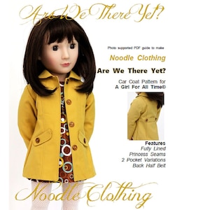 Könnte beinhalten: Eine Puppe in einem senfgelben Auto-Mantel mit braunen Knöpfen und Taschen, über einem braun-weiß gemusterten Kleid. Das Bild enthält den Text "Noodle Clothing" und "Are We There Yet?" Das Mantelmuster ist für ein Mädchen.