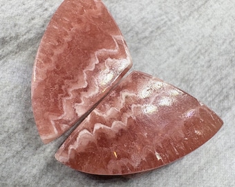 May include: Two pink and white, semi-circular, polished, natural stone cabochons with a wavy pattern.