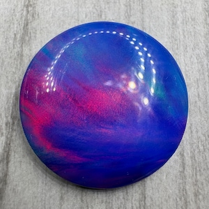 May include: A round, glossy object with a swirling pattern of blue, pink, and purple hues. The surface reflects light, creating bright spots. The object appears to be a decorative item or a piece of art.