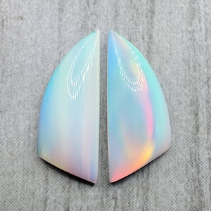 May include: Two iridescent, teardrop-shaped gemstones. The stones have a pearly white base with a shimmering rainbow effect. The gemstones are set against a gray textured background.