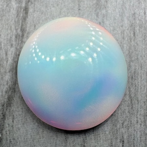 May include: A round, iridescent object with a smooth, glossy surface. The colors blend from pink to blue and green, creating a soft, ethereal appearance. The object appears to be made of glass or a similar material.