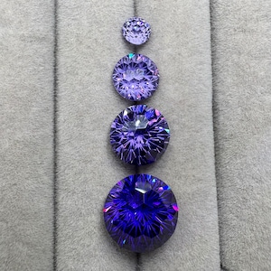 May include: Four round, faceted gemstones in varying sizes, arranged vertically. The gems transition in color from a light purple at the top to a deep blue at the bottom. Each stone has intricate internal facets, creating a sparkling effect.