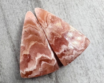 May include: Two pink and white triangular shaped cabochons of polished pink calcite. The cabochons have a swirling pattern of pink and white.