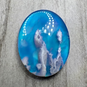 May include: An oval-shaped resin piece with a vibrant blue and white design. The blue hues transition from deep to light, resembling an ocean scene. White, cloud-like formations add depth and texture to the artwork.