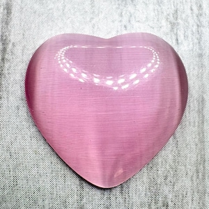 Peut inclure: Une pierre de cristal rose en forme de cœur. La pierre a une surface lisse et polie et une qualité translucide. Un motif en forme de cœur est gravé au centre de la pierre. Le cristal est posé sur un fond gris texturé.