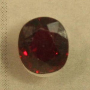 May include: A deep red oval-shaped gemstone with a smooth, polished surface.