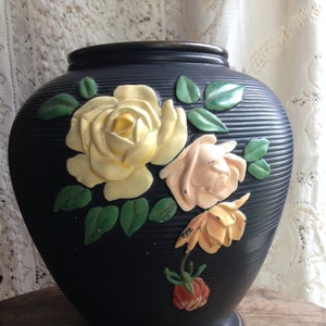 May include: A black ceramic vase with a raised floral design. The vase features yellow, pink, and orange roses with green leaves.