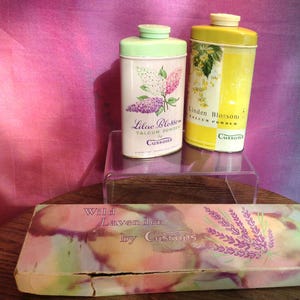 May include: Two vintage talcum powder tins with floral designs. The tin on the left is green and says "Lilac Blossom Talcum Powder by Cussons". The tin on the right is yellow and says "Linden Blossom Talcum Powder by Cussons". A box with a watercolour design says "Wild Lavender by Cussons".