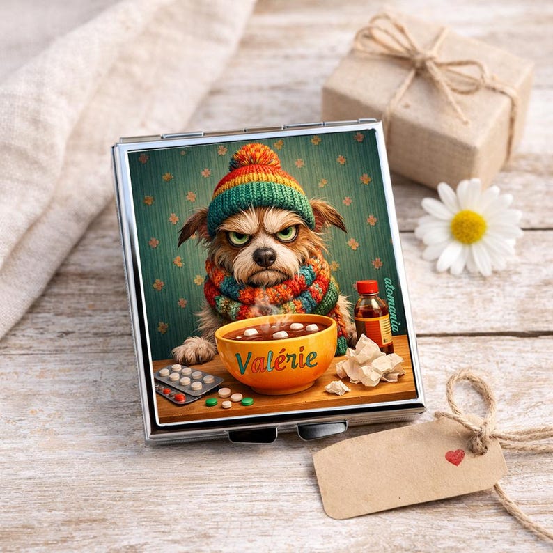 May include: A silver compact mirror featuring a grumpy dog wearing a colorful hat and scarf, with a bowl of soup and medicine. The word "Val&eacute;rie" is on the bowl. A gift box, daisy, and tag are in the background.