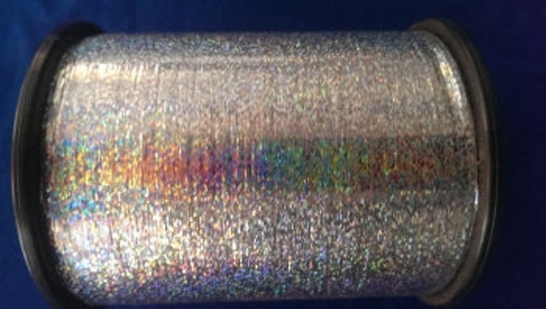 May include: A spool of silver iridescent metallic thread. The thread is shiny and has a holographic effect.