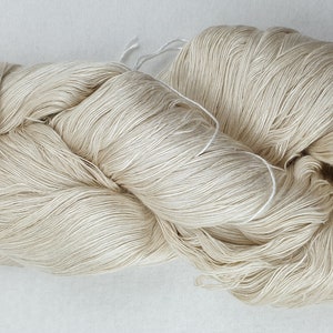 Può includere: Un gomitolo di filo color crema, realizzato in fibre naturali, è avvolto in modo lasco ed è pronto per essere lavorato a maglia o all'uncinetto.