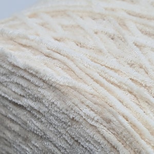 May include: A close-up of a skein of cream-colored yarn with a fuzzy texture. The yarn is tightly wound and has a soft, fluffy appearance.