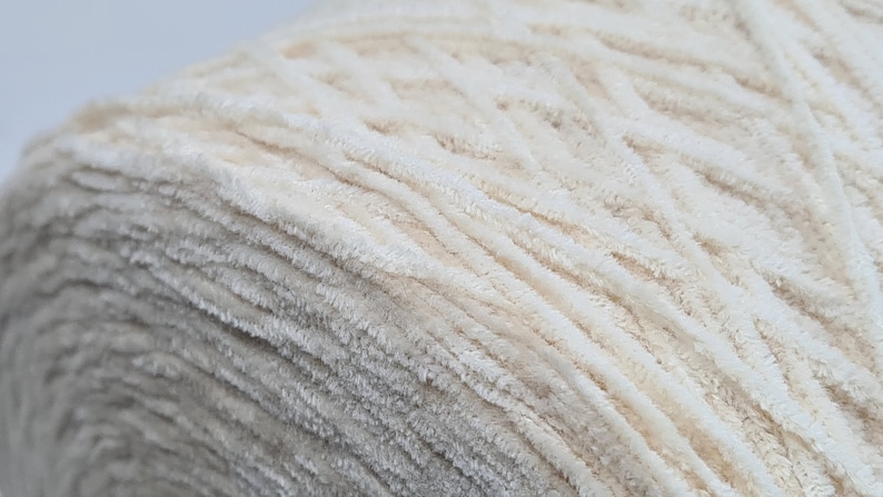 May include: A close-up of a skein of cream-colored yarn with a fuzzy texture. The yarn is tightly wound and has a soft, fluffy appearance.