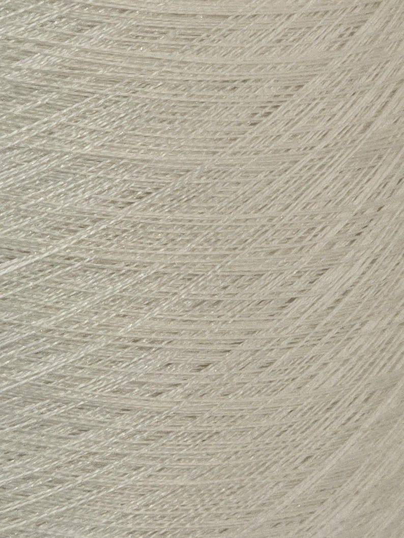 May include: A close-up of a spool of light beige yarn.