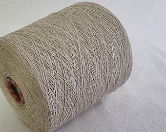 Könnte beinhalten: Eine Spule mit natürlichem Leinen Garn, fest gewickelt und bereit zum Stricken oder Häkeln. Das Garn ist hellbeige und hat einen dezenten Glanz.
